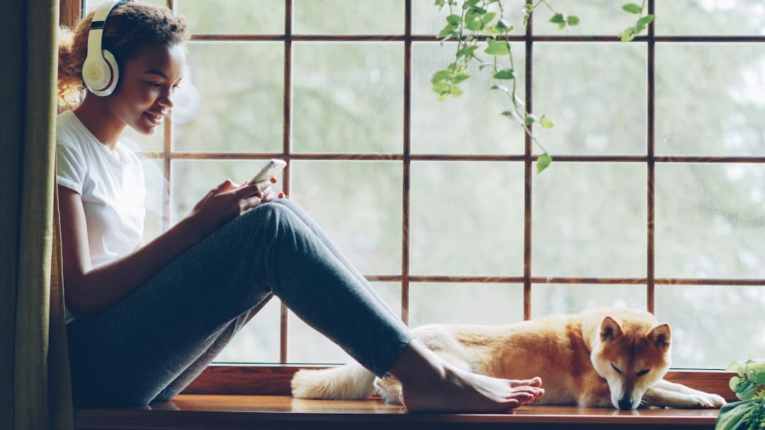 PTSD service dog — Woman listens to music with her dog by the window.